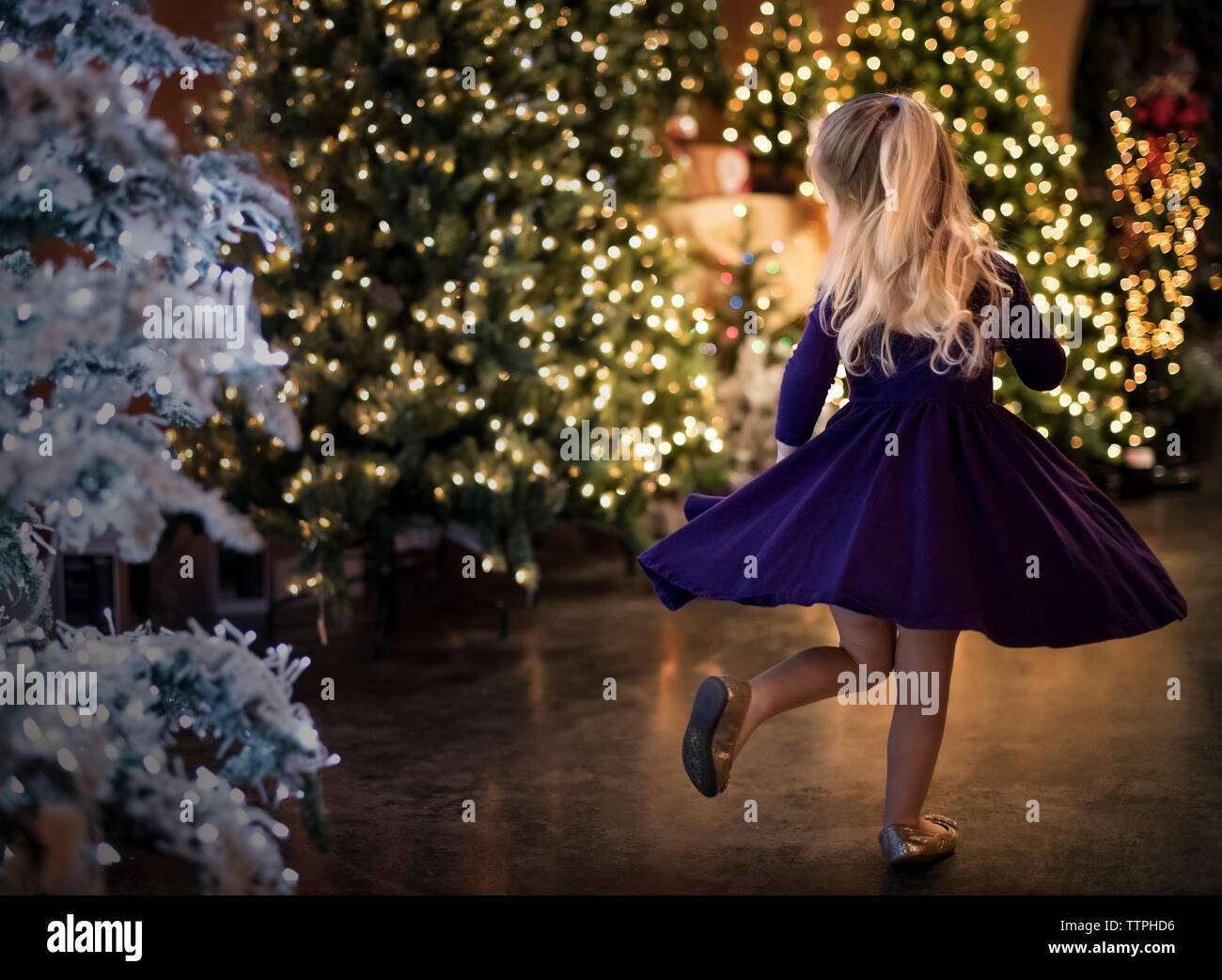 Rückansicht eines glücklichen Mädchens, das nachts an beleuchteten weihnachtsbäumen tanzt Stockfoto