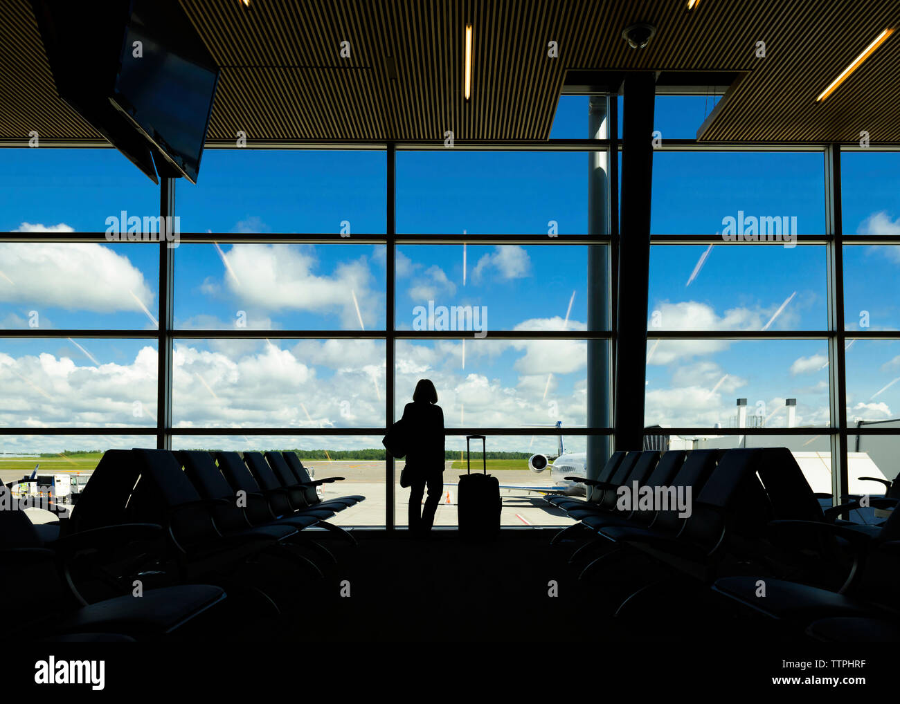 Silhouette Frau mit Koffer stehend gegen Fenster am Flughafen Stockfoto