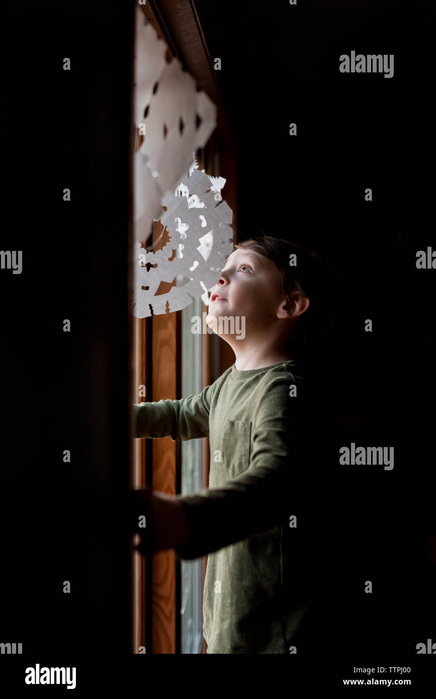 Ein kleiner Junge zu Papier Schneeflocken in einem Fenster Stockfoto