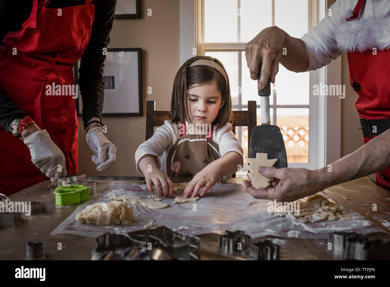 Enkelin hilft Großeltern, weihnachtskekse auf dem Tisch zu machen Stockfoto