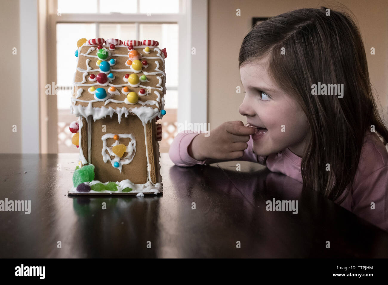 Glücklich mit dem Finger im Mund auf der Suche nach Gingerbread House auf dem Tisch zu hause Cute Stockfoto