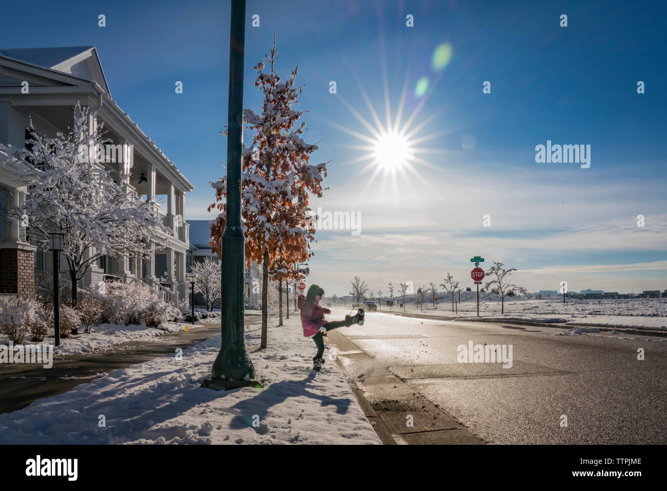 Seitenansicht des verspielten Mädchen kicken Schnee auf der Straße gegen den blauen Himmel während der sonnigen Tag Stockfoto