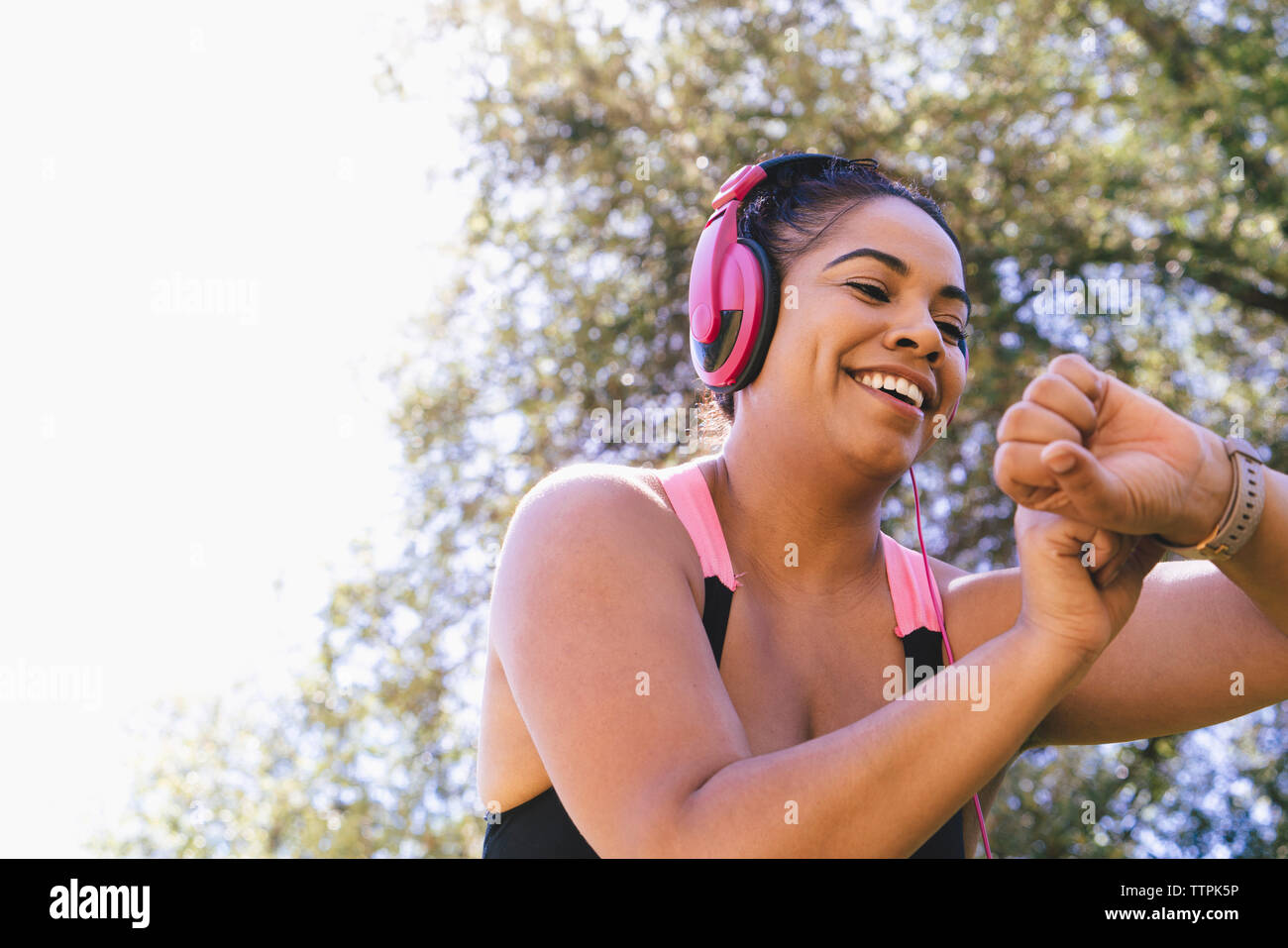 Low Angle View der glücklichen Frau auf der Suche nach Fitness Tracker beim Hören von Musik im Park Stockfoto