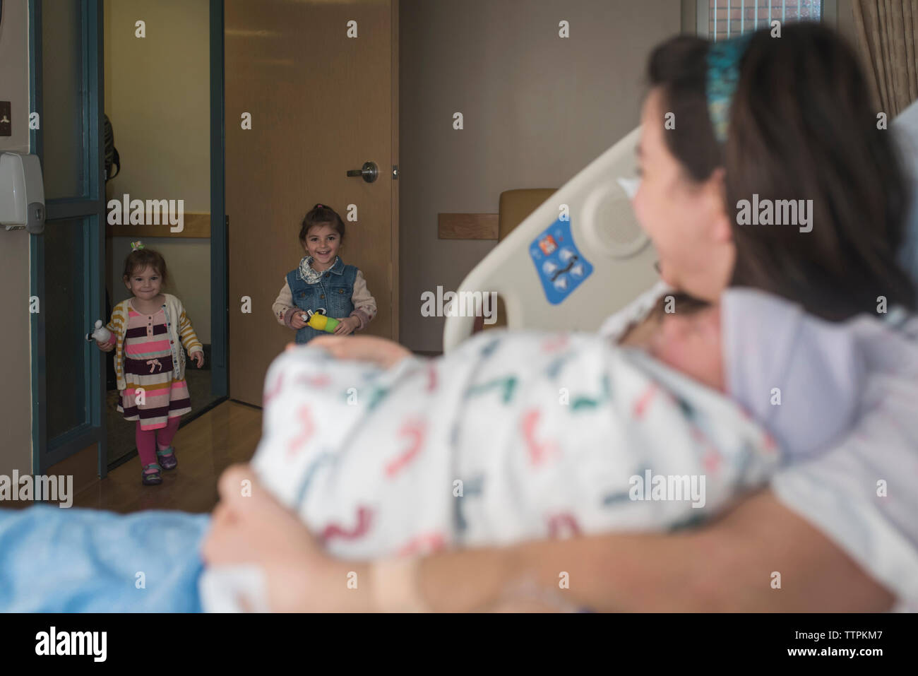 Mutter Holding neugeborenen Sohn betrachten Töchter in die Krankenstation, während sie sich auf dem Bett Stockfoto