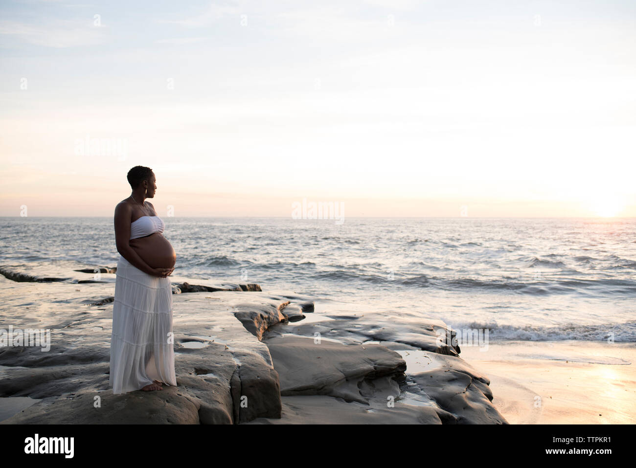 Schwangere Frau am Strand gegen Himmel bei Sonnenuntergang Stockfoto