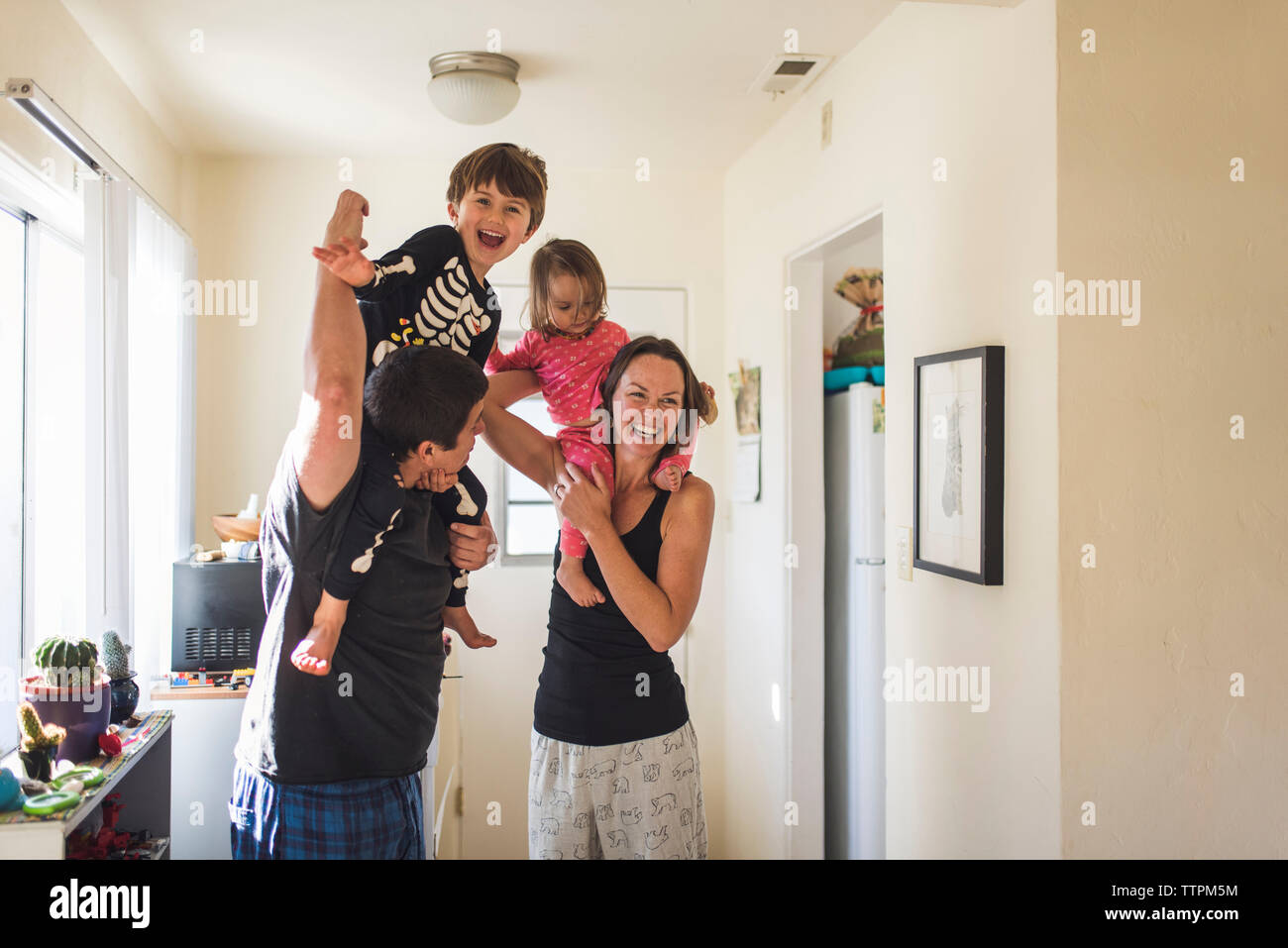 Glückliche Eltern, die Kinder auf den Schultern während zu Hause stehend Stockfoto