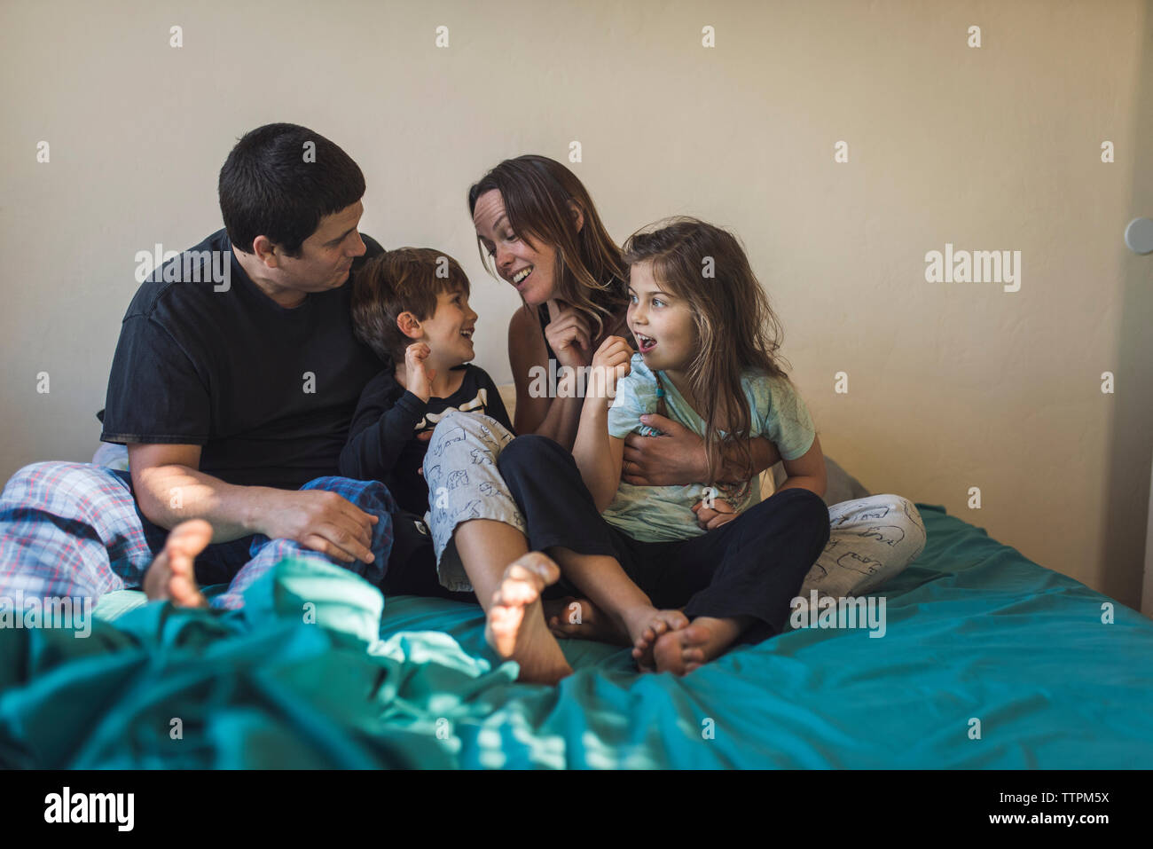 Glückliche Eltern spielen mit den Kindern auf dem Bett zu Hause. Stockfoto
