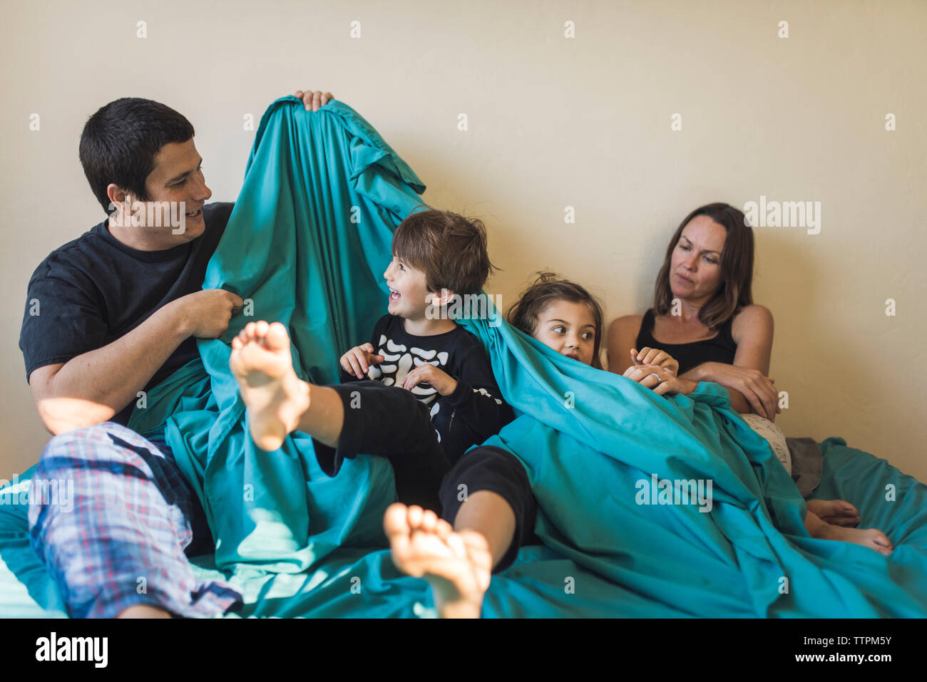 Glückliche Eltern spielen mit den Kindern, während auf dem Bett zu Hause sitzen Stockfoto