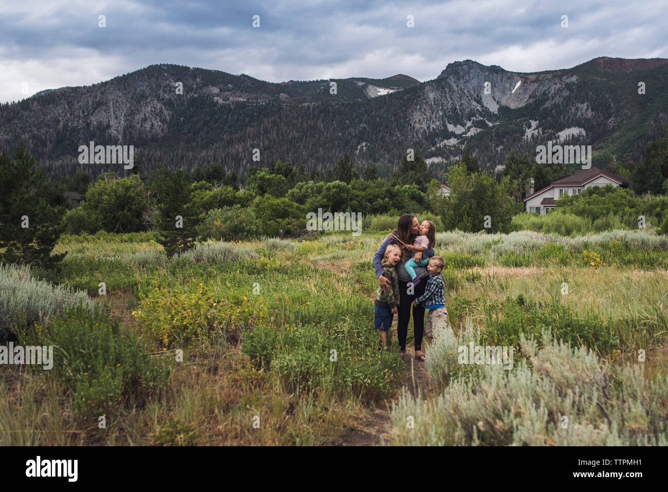 Glückliche Mutter mit Kindern stehen auf gras landschaft gegen bewölkter Himmel im Wald Stockfoto