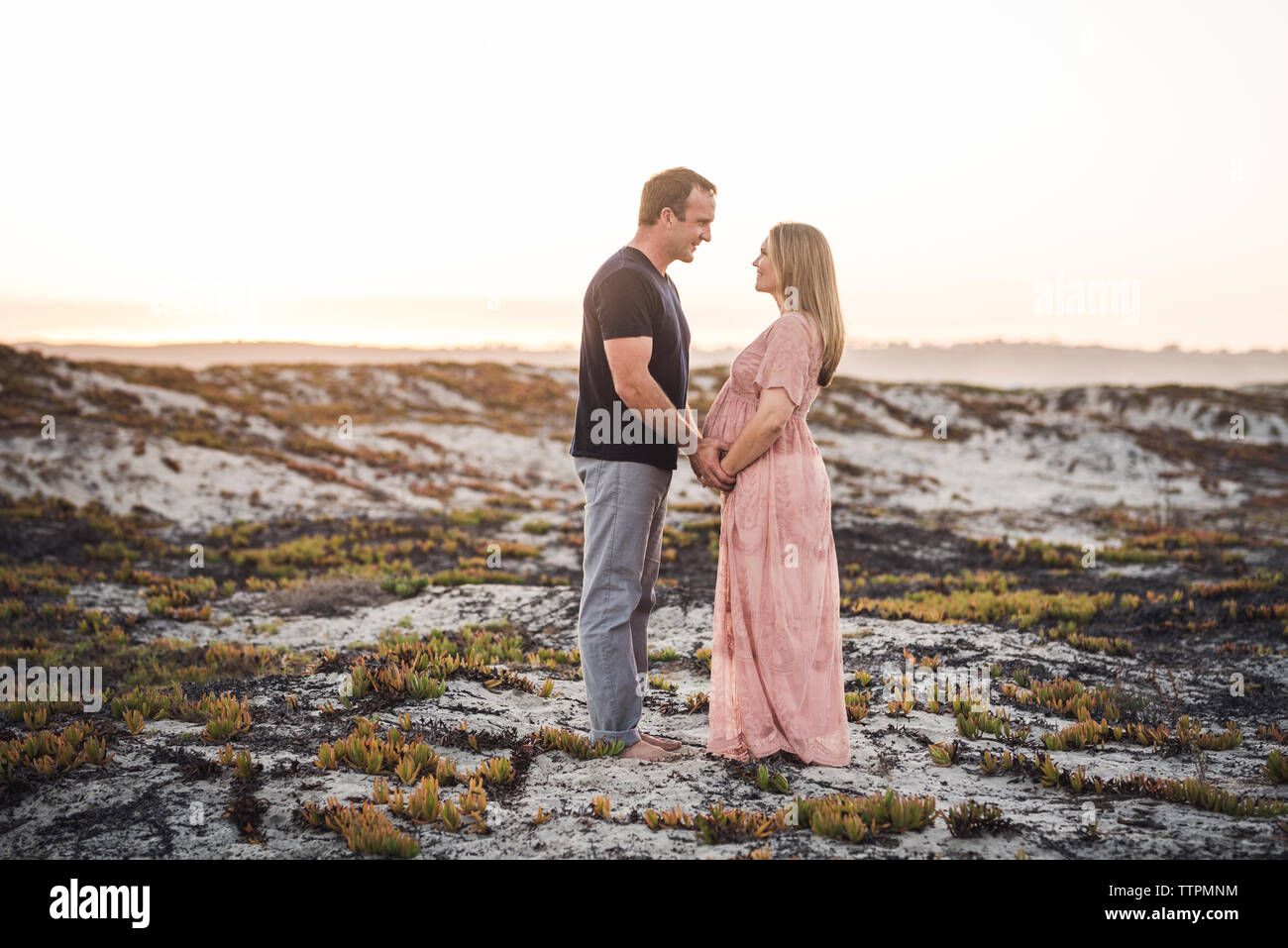Seitenansicht des Romantisches Paar sich einander beim Stehen am Strand gegen den klaren Himmel bei Sonnenuntergang Stockfoto