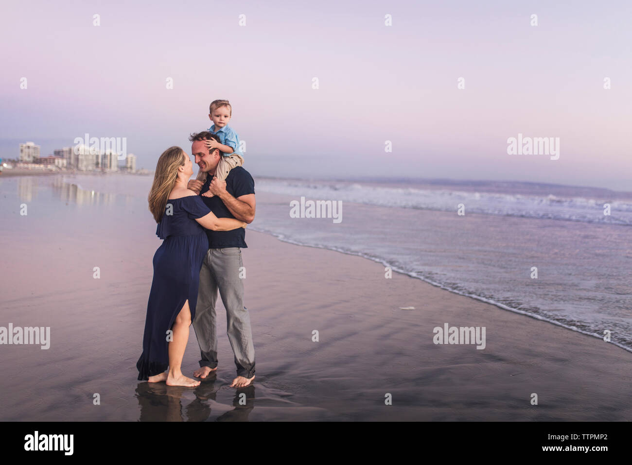 Romantische Mann sucht bei Frau, während der Sohn am Strand gegen Himmel bei Sonnenuntergang Stockfoto