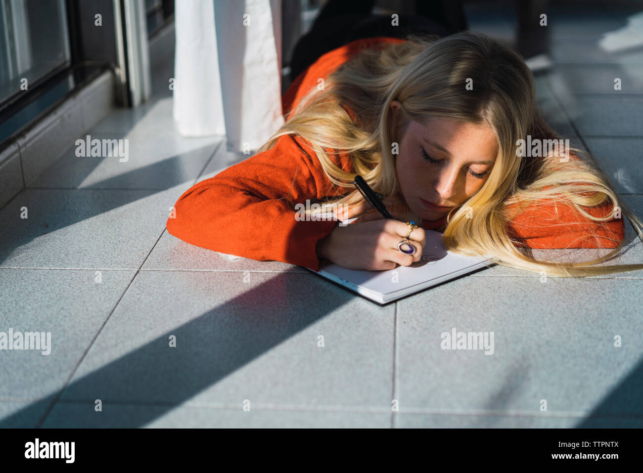 Junge Frau Skizzieren auf Buch, während auf gefliestem Boden zu Hause liegen Stockfoto