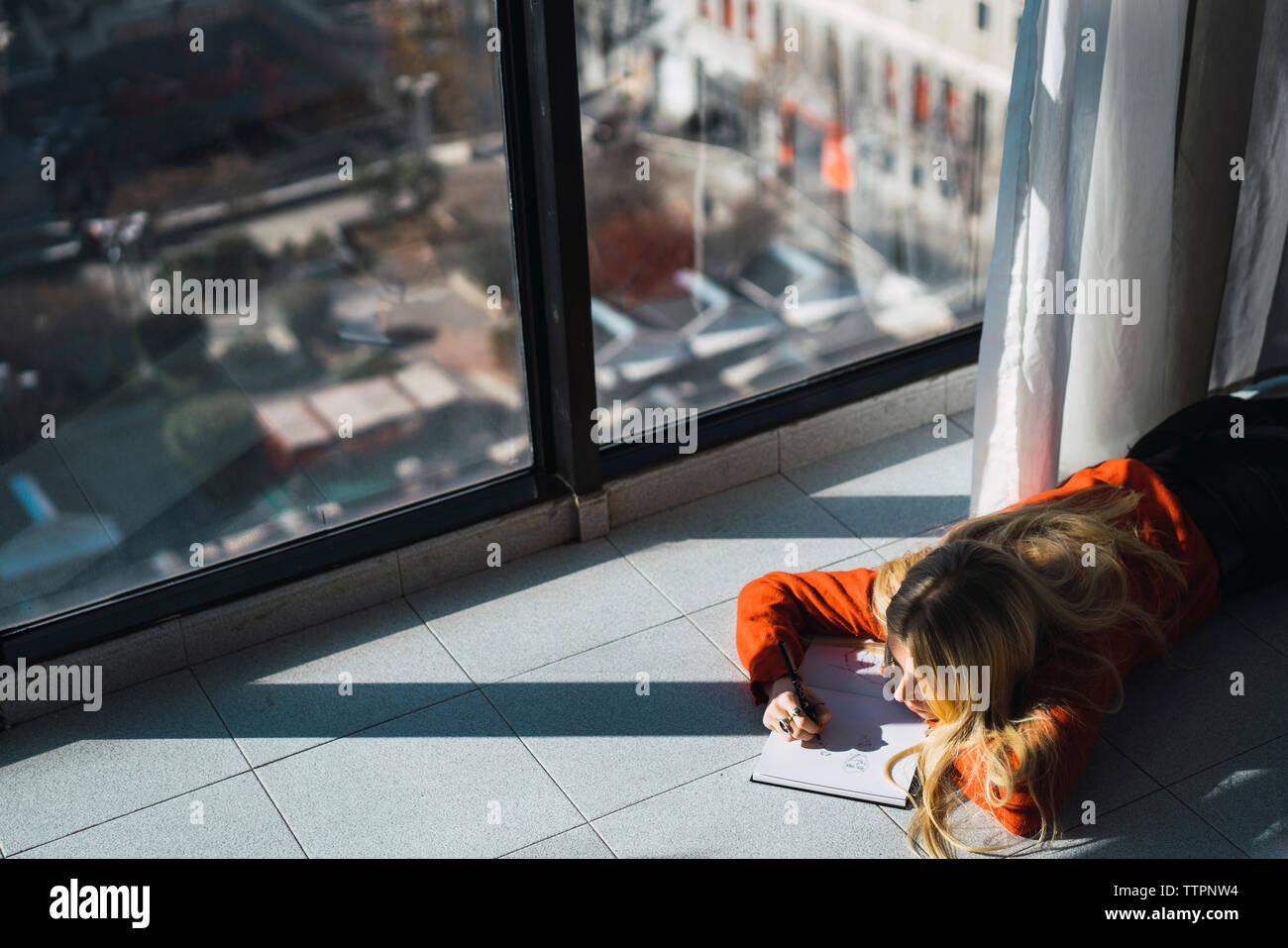 Hohe Betrachtungswinkel und der jungen Frau Skizzieren auf Buchen Sie beim Lügen auf gefliestem Boden zu Hause Stockfoto