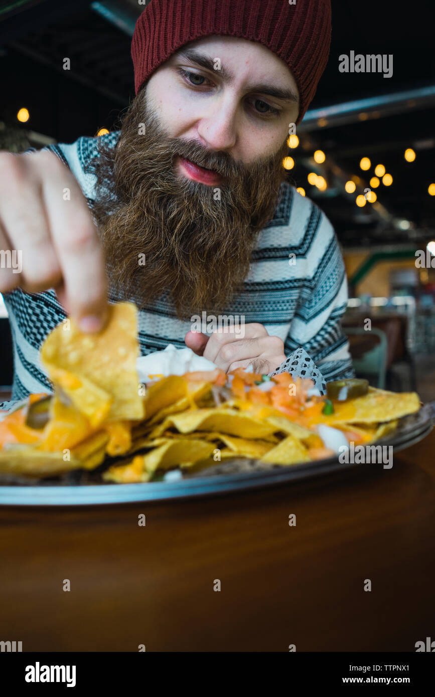 Hipster Mann die Tortilla Chip von der Platte auf dem Tisch im Cafe Stockfoto