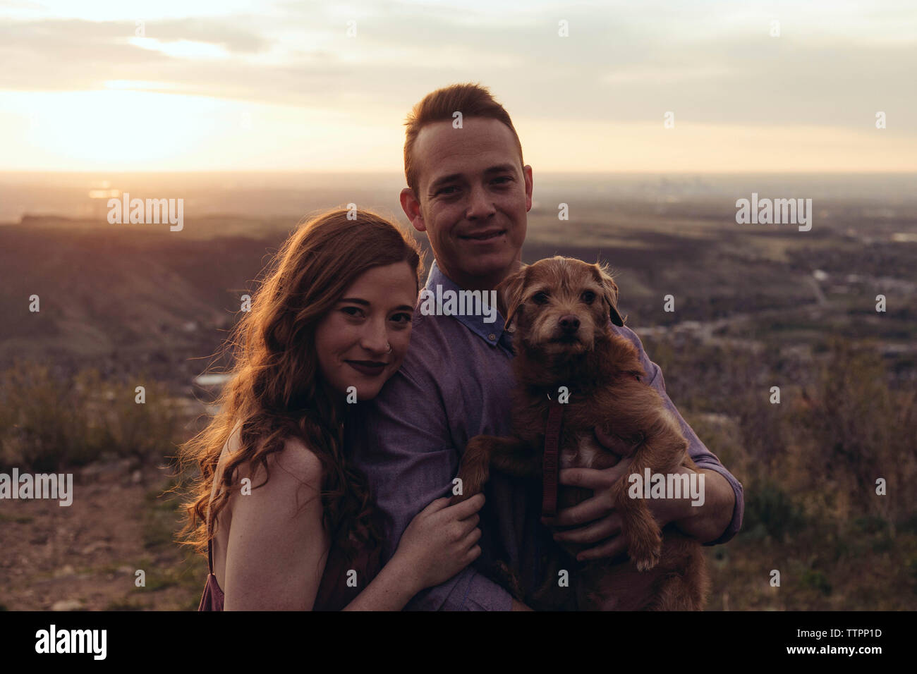 Portrait von junges Paar mit Hund stehend auf dem Feld bei Sonnenuntergang Stockfoto