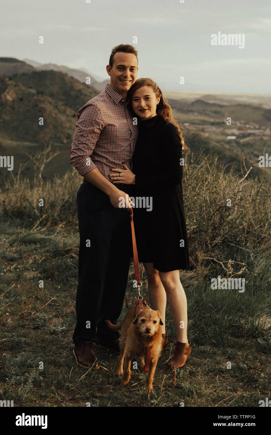 Volle Länge Portrait von junges Paar mit Hund stehend auf dem Feld bei Sonnenuntergang Stockfoto