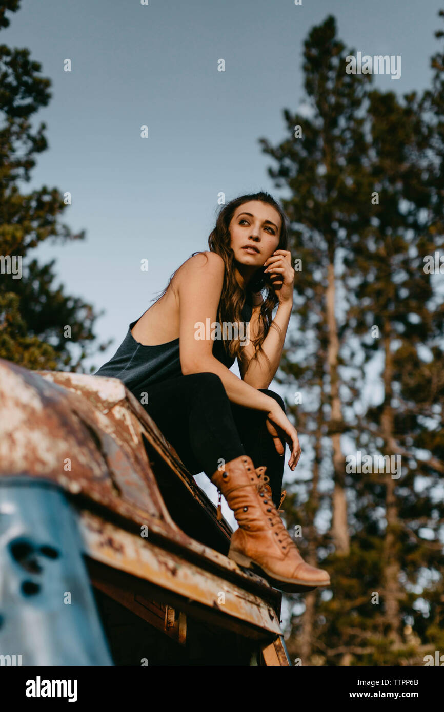 Low Angle View von nachdenklich junge Frau sitzt auf der verlassenen Fahrzeug im Wald Stockfoto