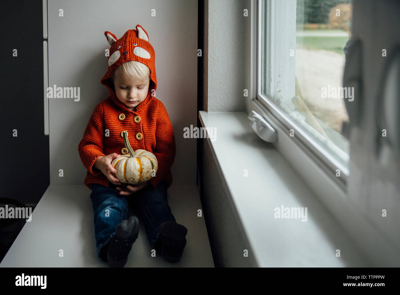 Süße Junge mit Kürbis, während durch die Fenster während der Halloween zu Hause sitzen Stockfoto