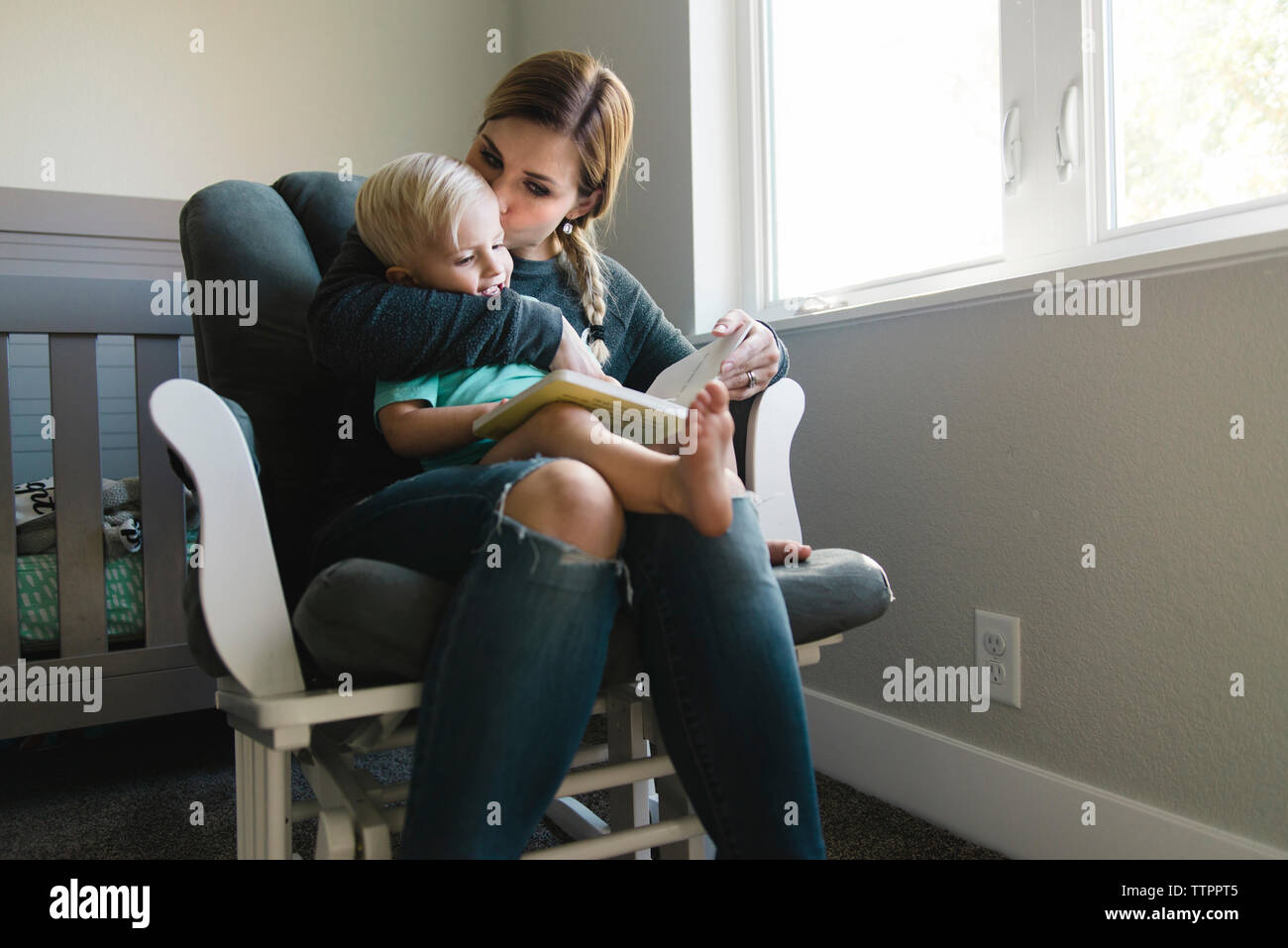 Mutter küssen Sohn während Buch auf dem Stuhl zu Hause lesen Stockfoto
