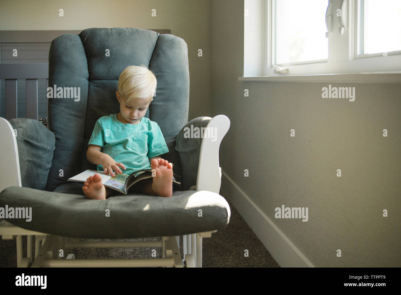 Junge lesen Buch beim Sitzen auf Stuhl zu Hause Stockfoto