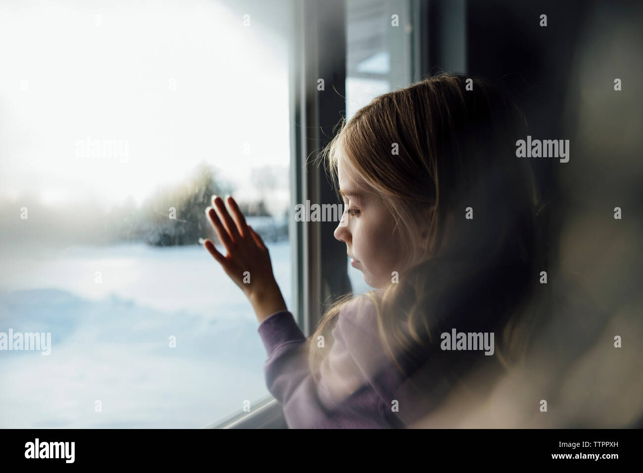 Nachdenklich stehendes Mädchen durch Fenster zu Hause Stockfoto