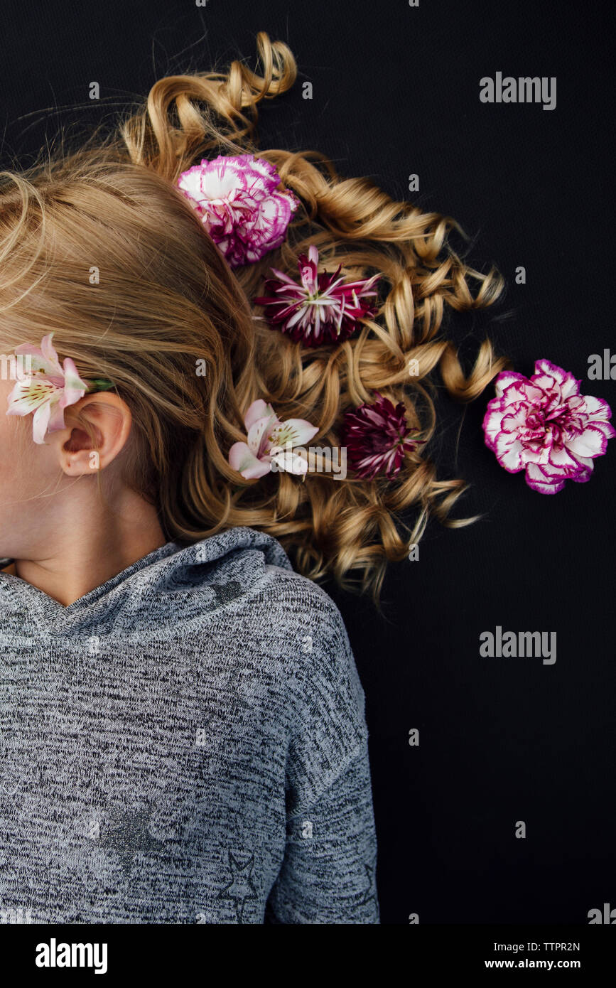 Ansicht von oben von Mädchen mit Blumen im Haar beim Liegen auf schwarzem Hintergrund Stockfoto