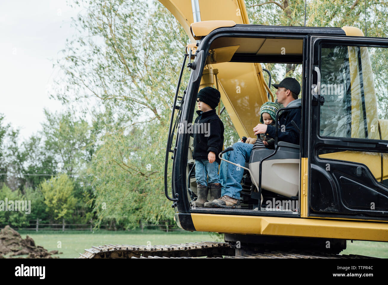 Vater mit Söhnen sitzt im earthmovers auf Feld Stockfoto