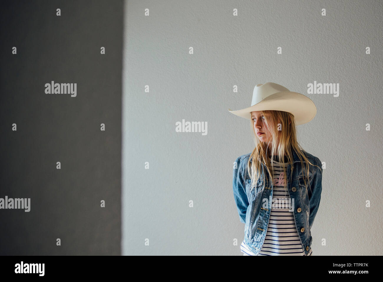 Nachdenkliches Mädchen mit Hut stehend gegen Wand Stockfoto
