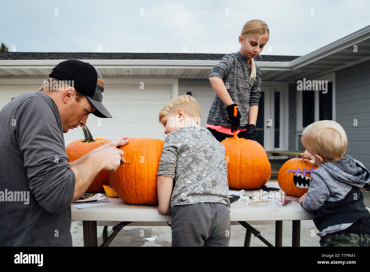 Vater mit Kindern schneiden Kürbis am Tisch im Hinterhof während der Halloween Stockfoto