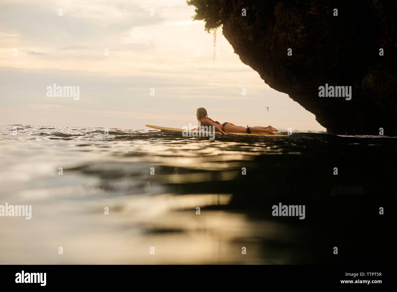 Seitenansicht der Frau Wellenreiten im Meer bei Sonnenuntergang Stockfoto