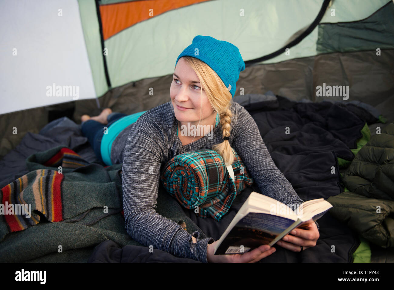 Lächelnde Frau mit Buch, während im Zelt liegend Stockfoto