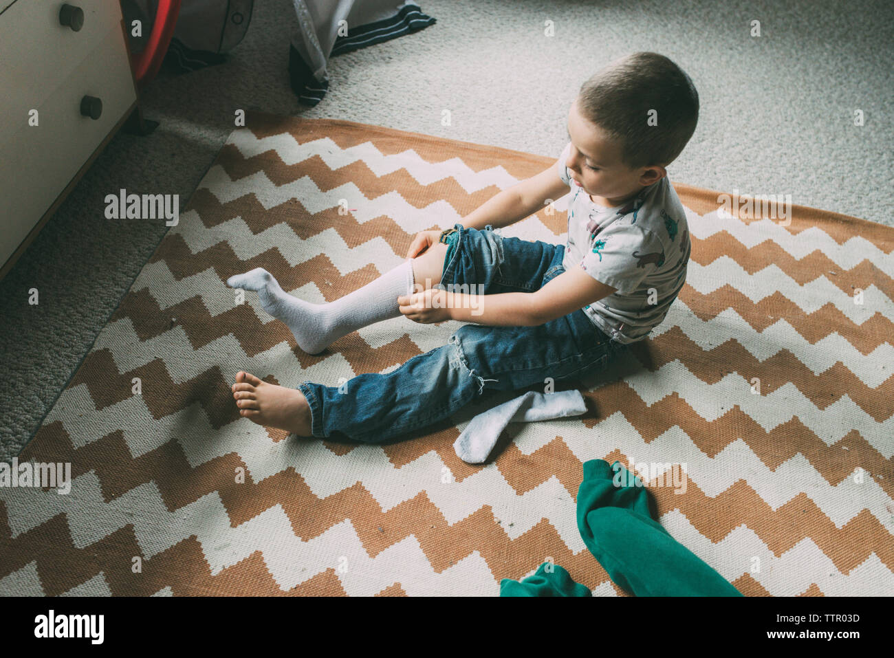 Hohe Betrachtungswinkel der Boy ziehen an Socke beim Sitzen auf dem Teppich zu Hause Stockfoto