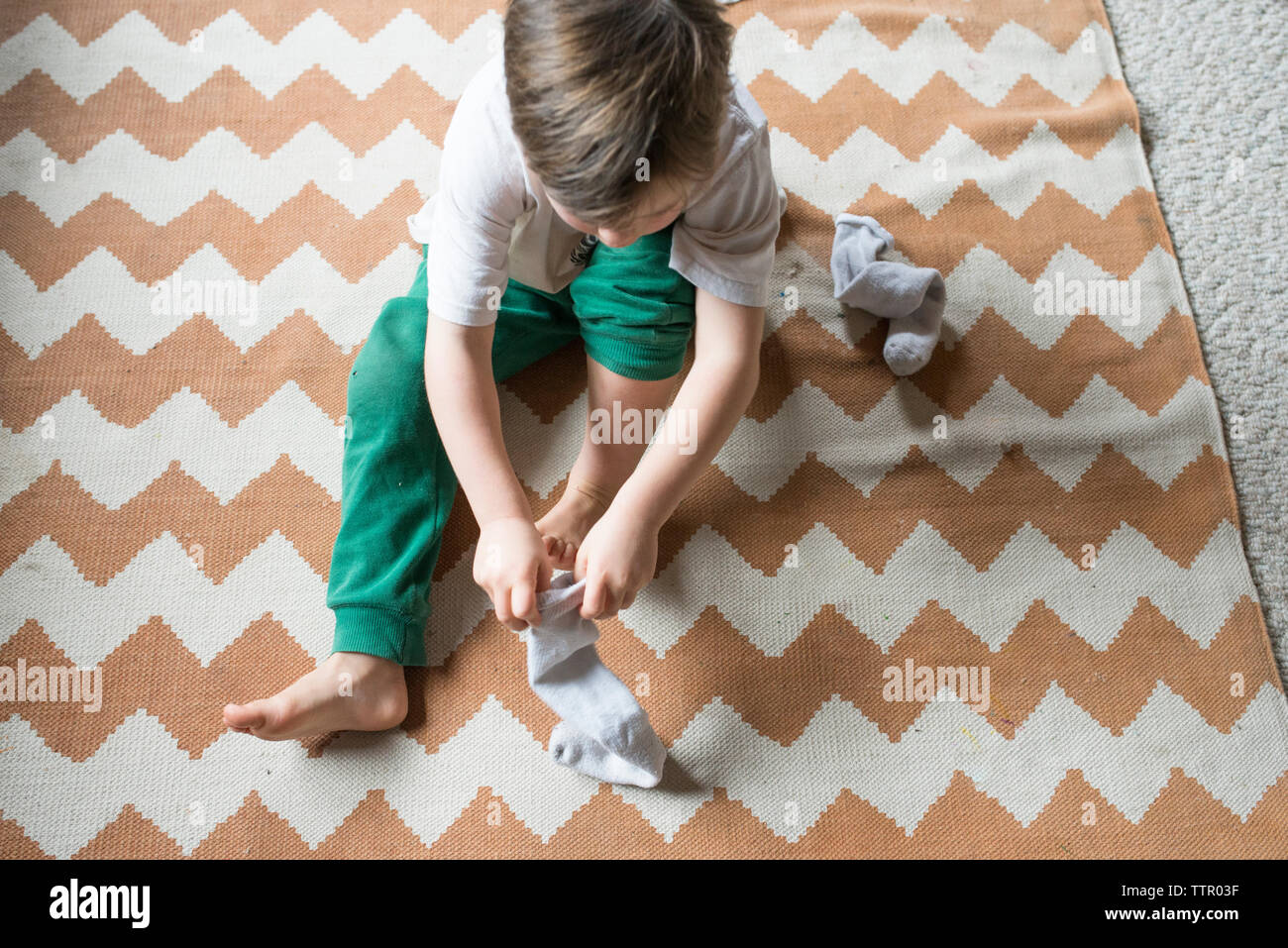 Hohe Betrachtungswinkel und der Junge trägt Socken beim Sitzen auf dem Teppich zu Hause Stockfoto