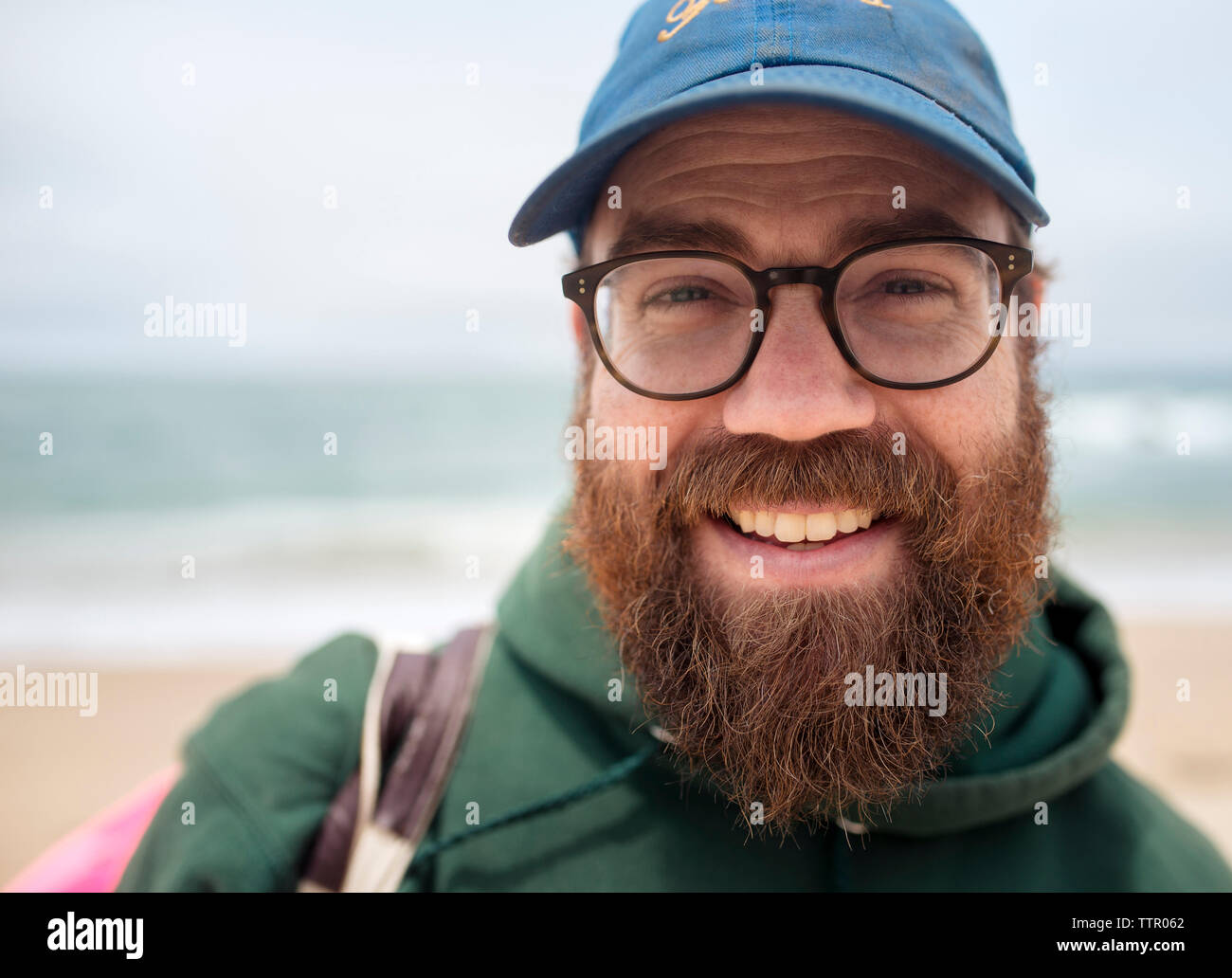 Close-up Portrait von lächelnden bärtigen Mann mit Mütze und Brille am Strand Stockfoto