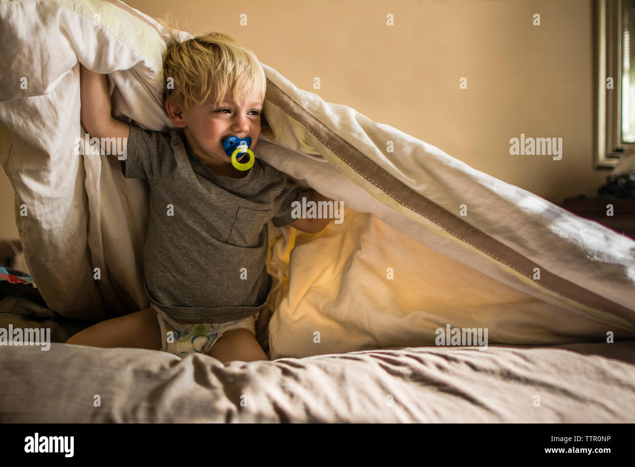 Junge mit Schnuller im Mund schreien während Knien auf dem Bett Stockfoto
