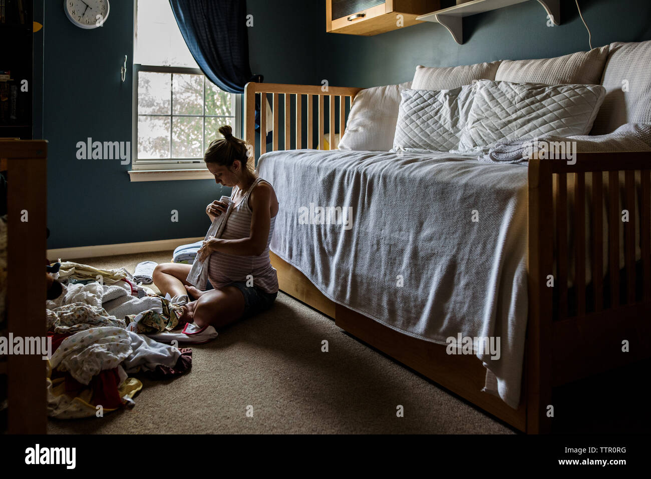 Die werdende Mutter sitzt auf Kindergarten, falten Baby Kleidung Stockfoto