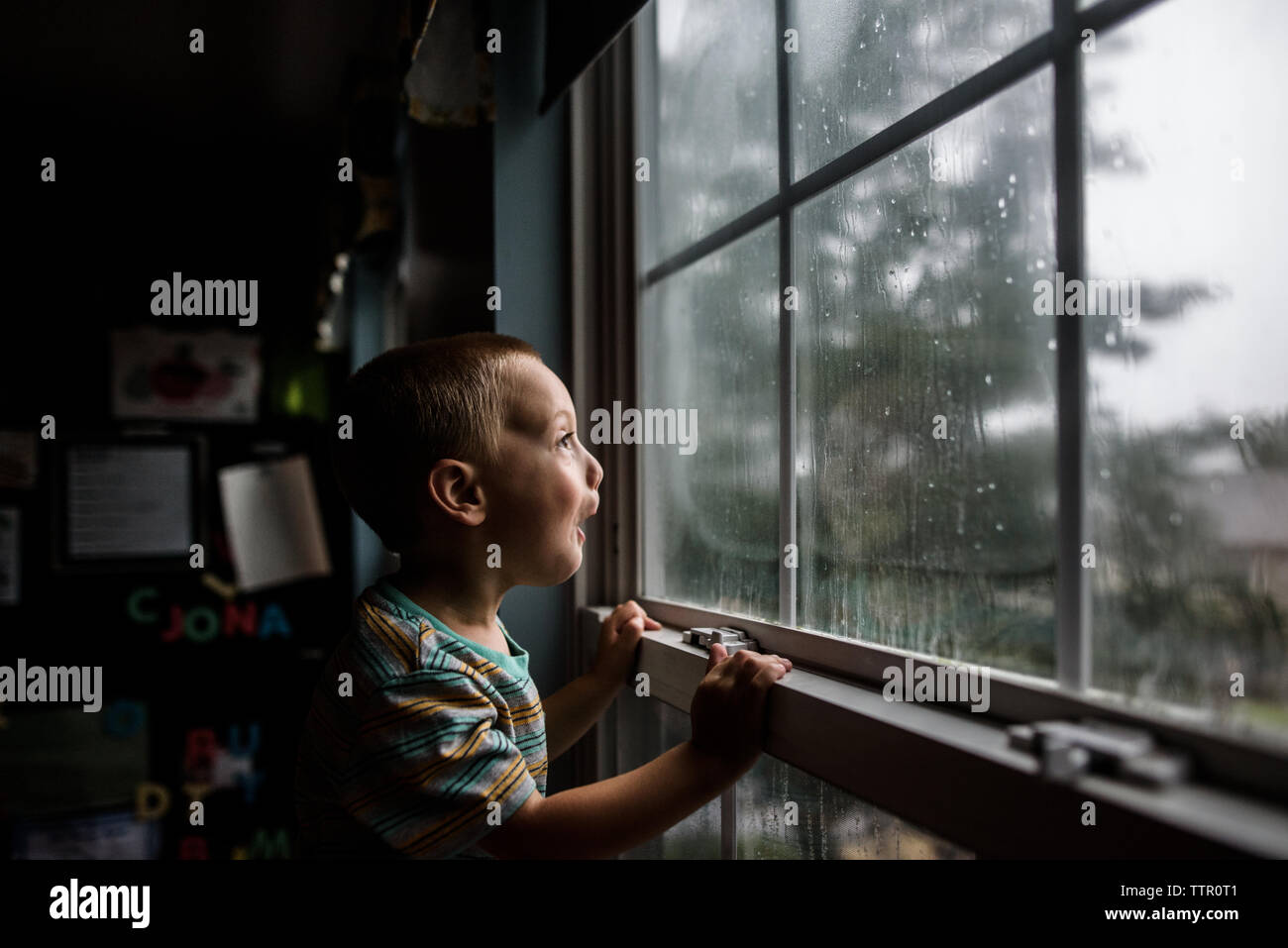 Begeistert junge auf der Suche nach einem Fenster mit Regentropfen an einem stürmischen Himmel Stockfoto