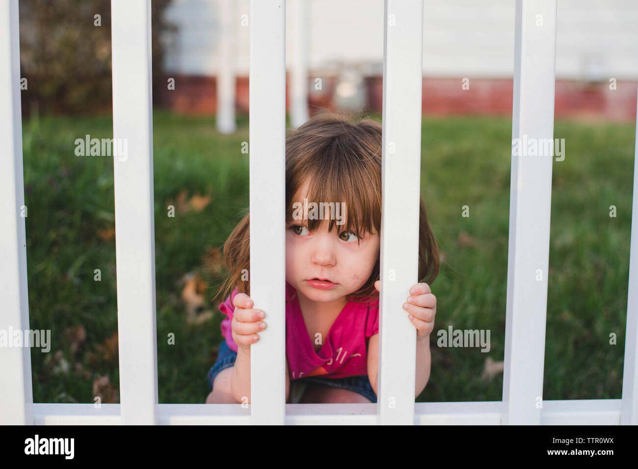 Süße Mädchen schauen durch Zaun im Hinterhof Stockfoto