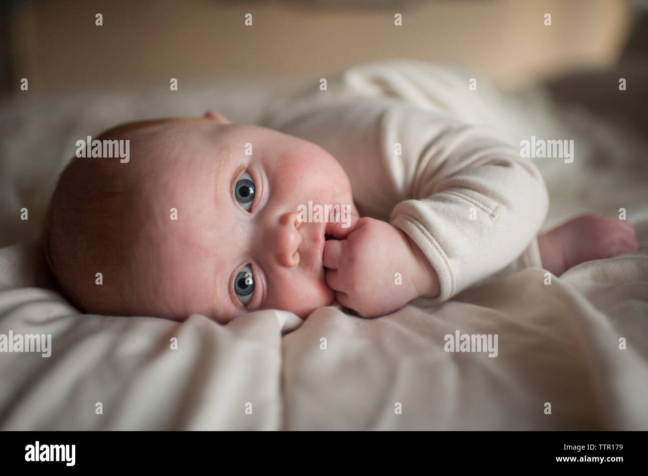 Portrait von cute baby boy mit Finger im Mund liegend auf Bett Stockfoto