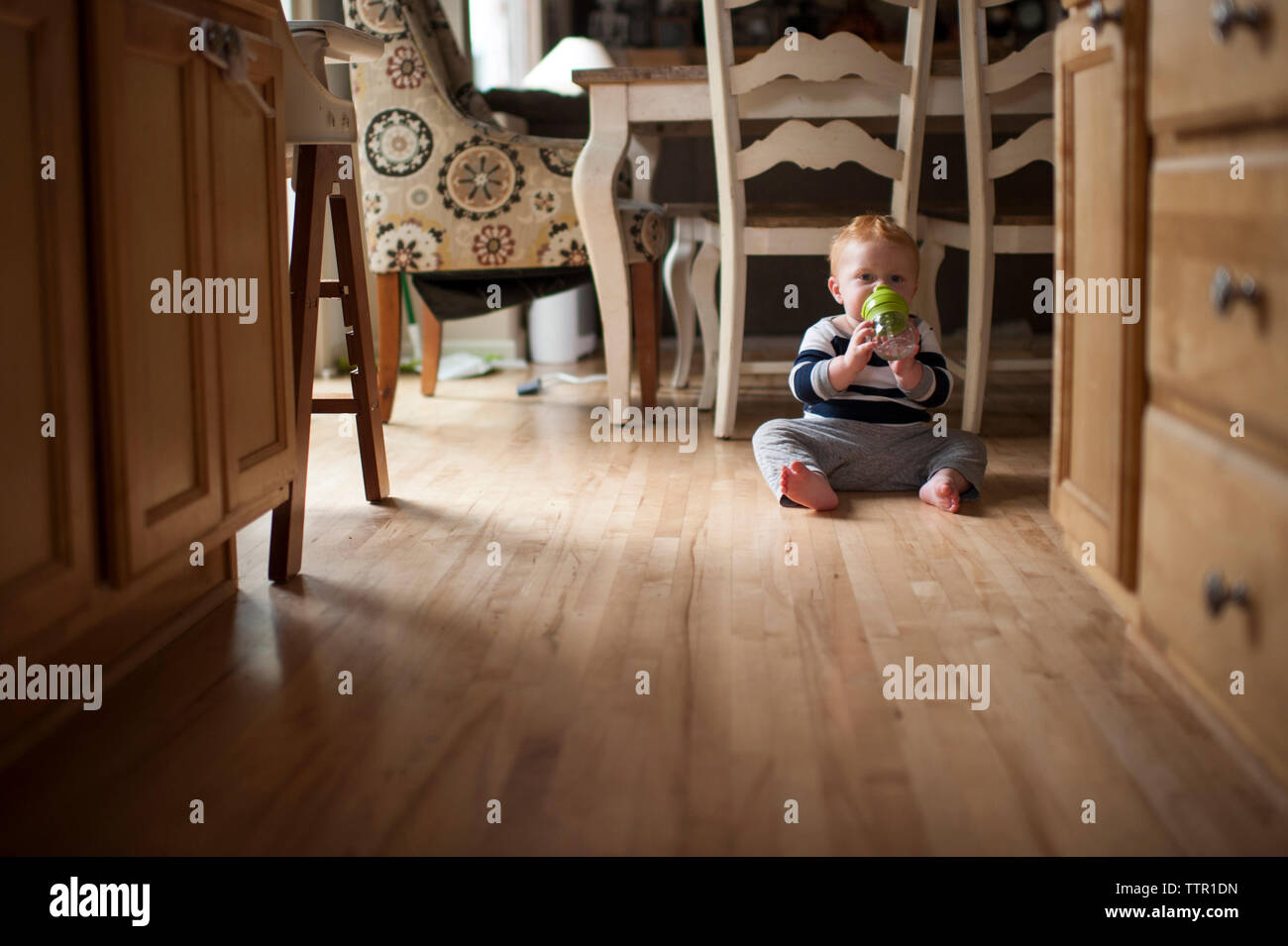 Portrait von baby boy Trinkwasser aus der Flasche beim Sitzen auf dem Boden zu Hause Stockfoto