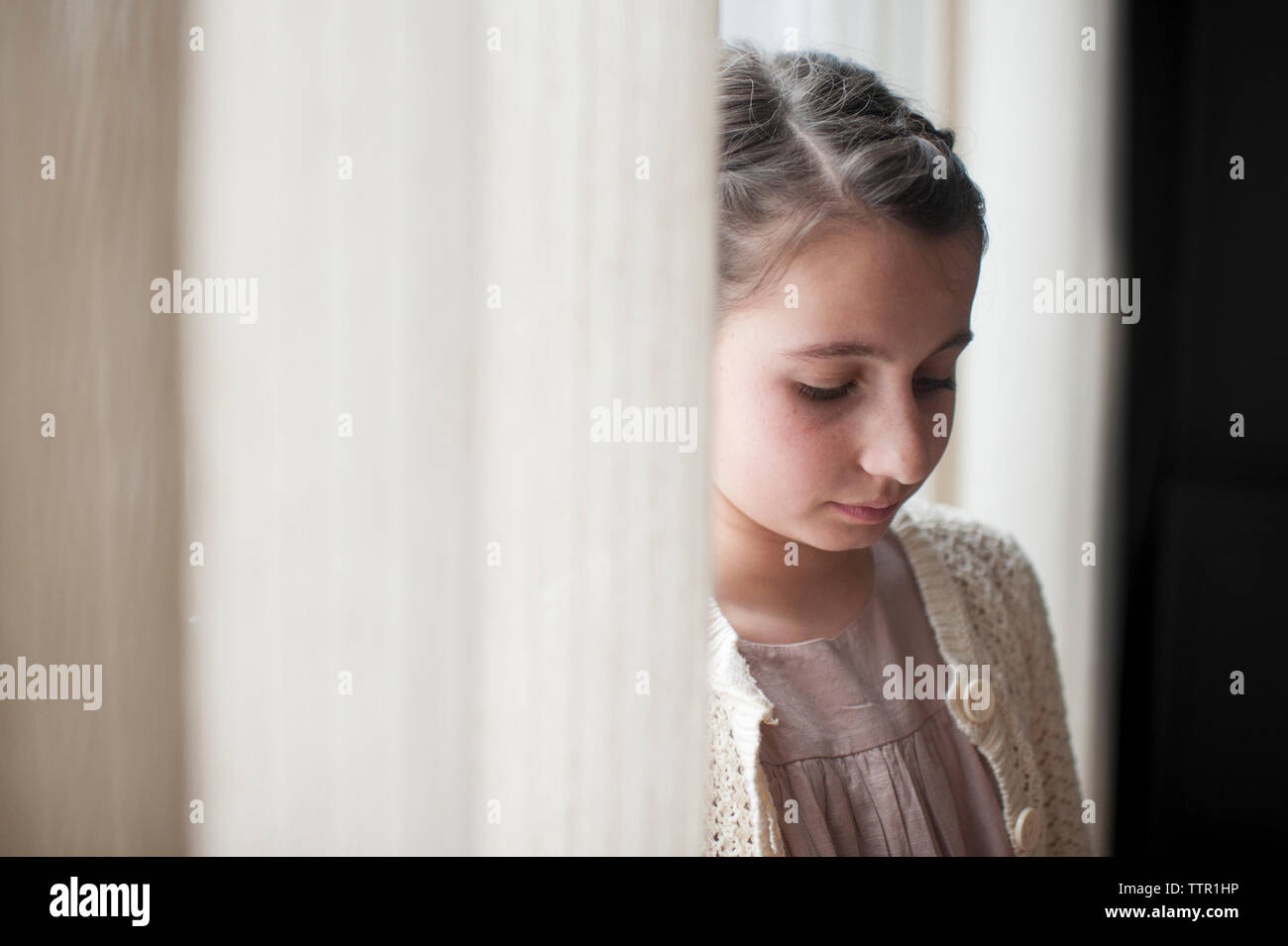 Trauriges Mädchen von Vorhängen zu Hause Stockfoto
