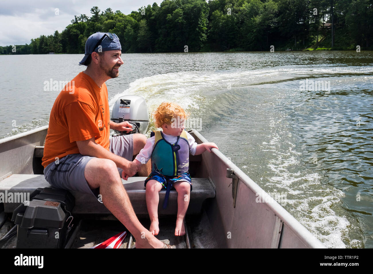 Vater und Sohn genießen die Fahrt mit dem Motorboot in See am Wald Stockfoto