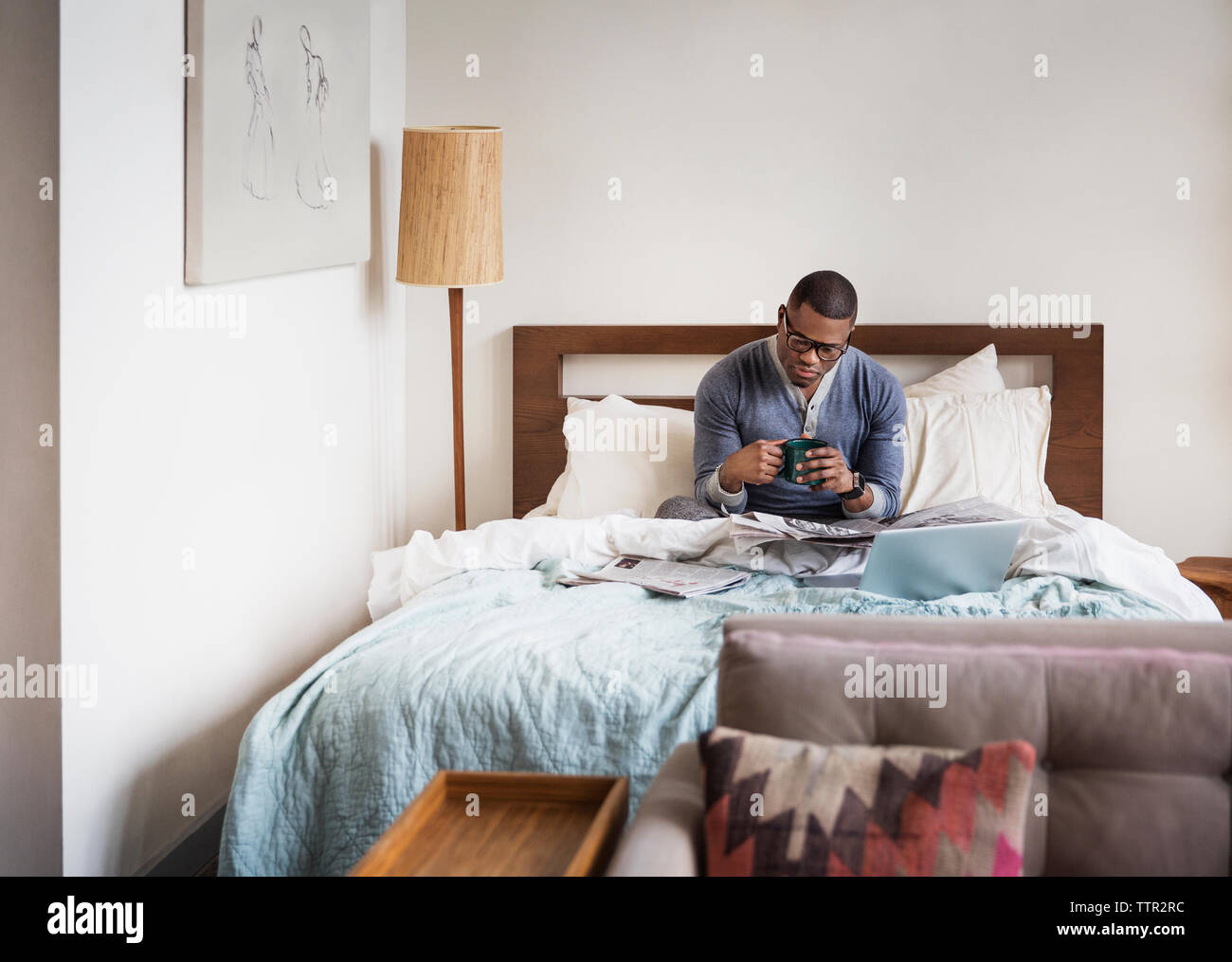 Mann mit Tasse Kaffee beim Lesen der Zeitung auf Bett zu Hause Stockfoto