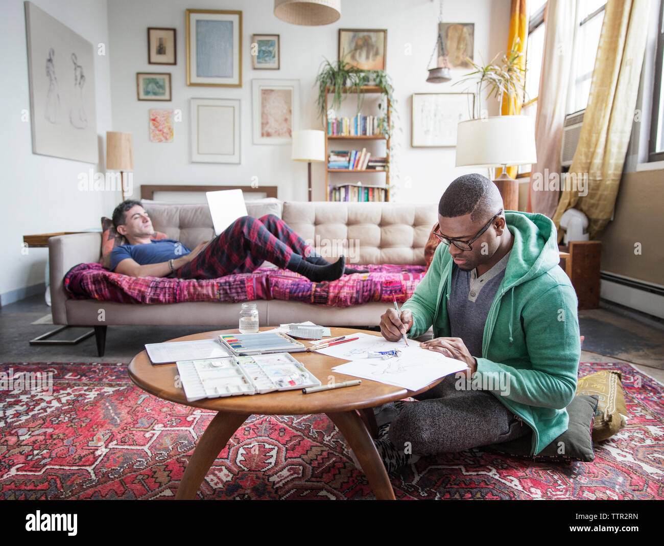 Homosexueller mann Zeichnung während der Partner mit Laptop zu Hause Stockfoto