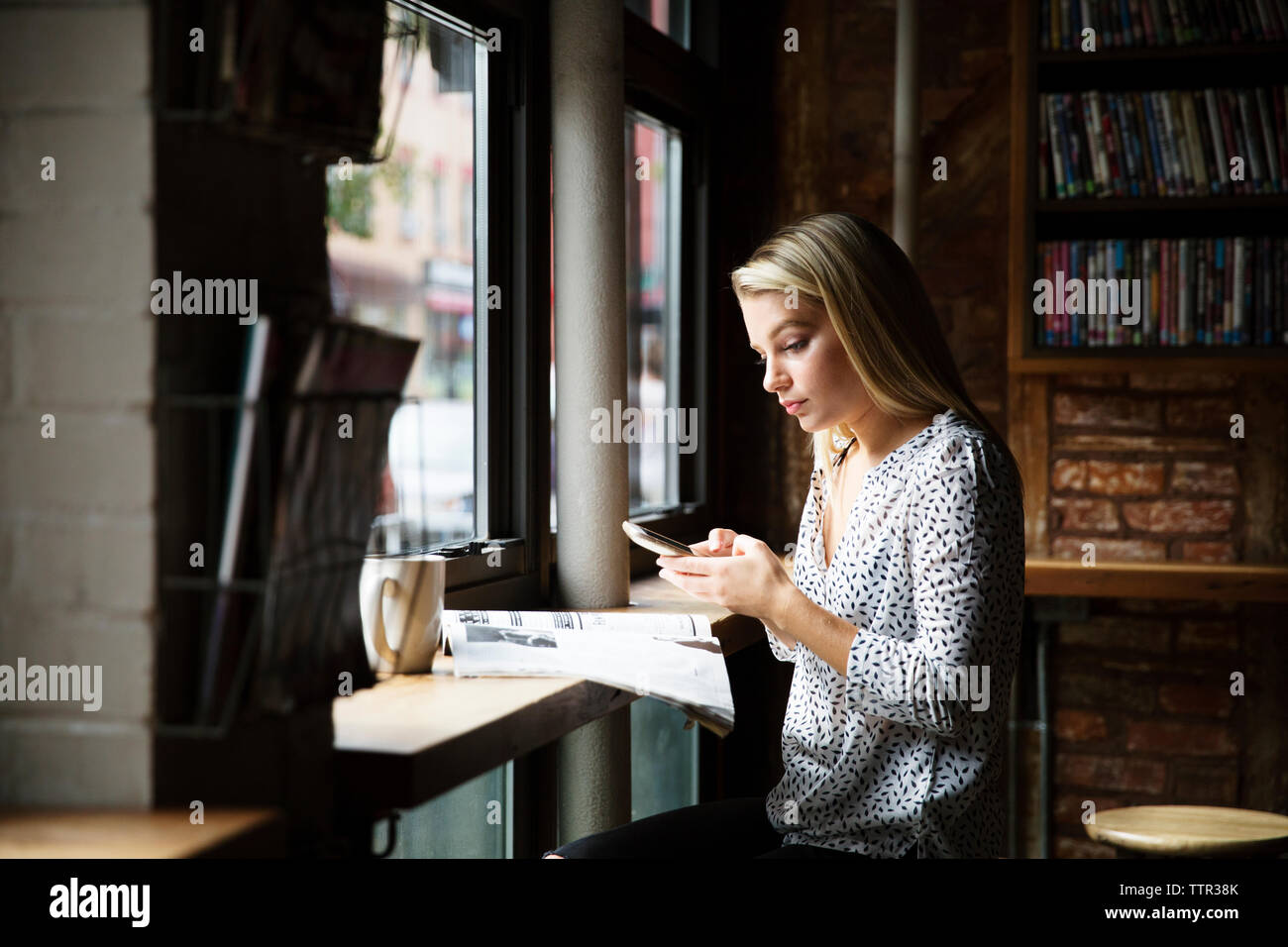 Junge Frau mit Phone beim Lesen der Zeitung an den Tisch im Cafe Stockfoto