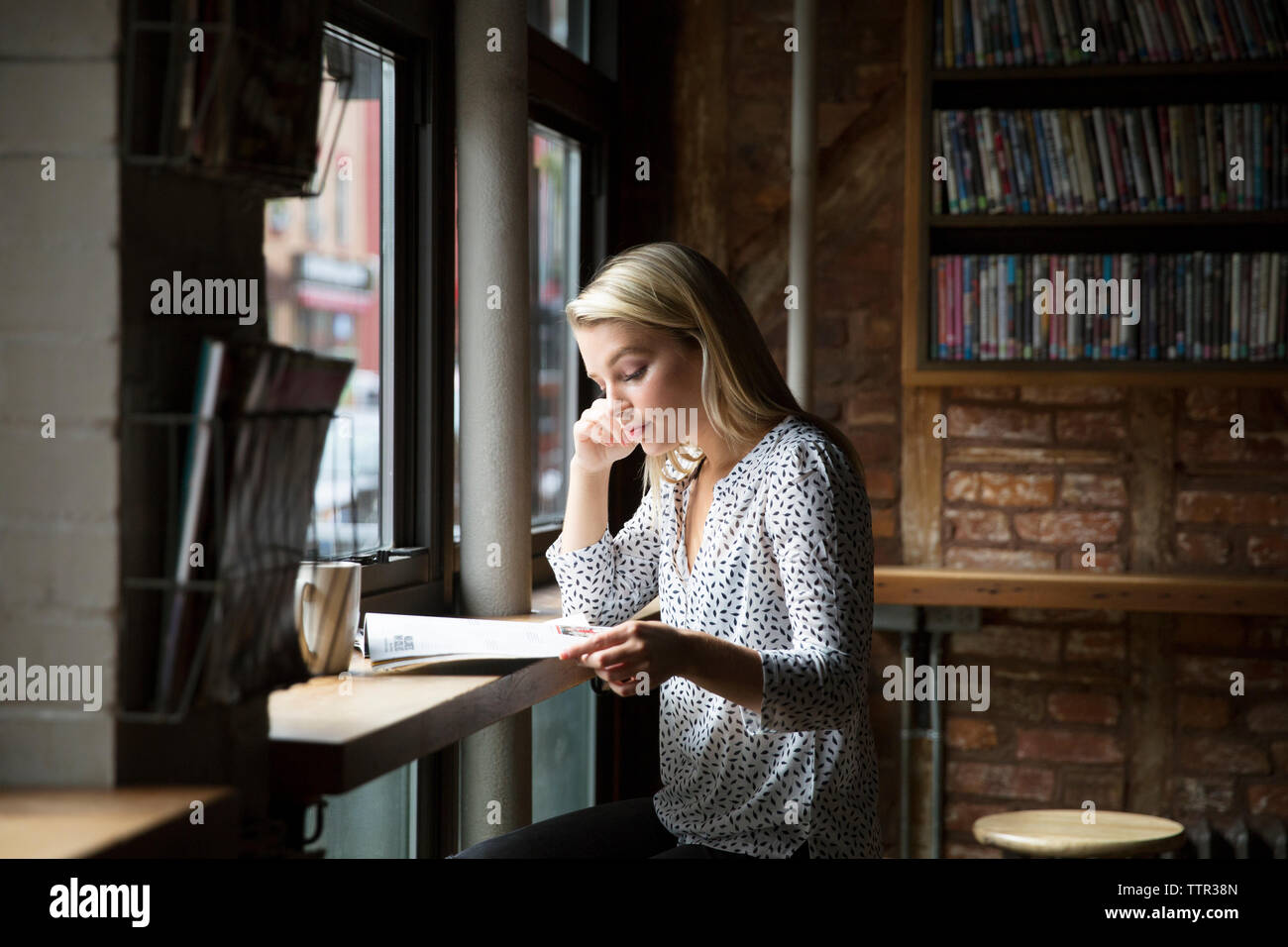 Ernsthafte Frau liest Zeitung durch Schale auf dem Tisch im Cafe Stockfoto