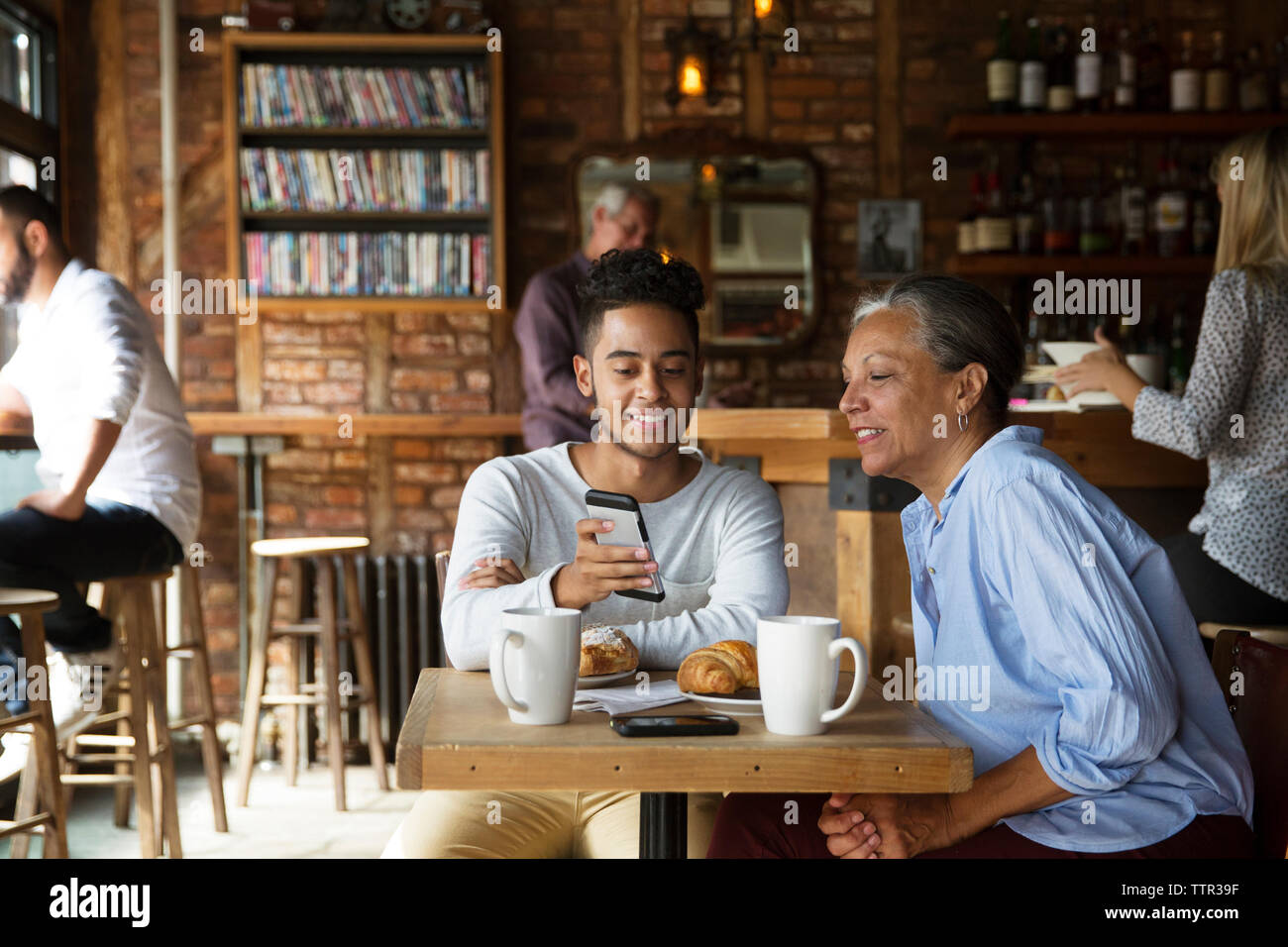 Lächelnder Mann mit Telefon an Frau beim Kunden Entspannung im Cafe Stockfoto