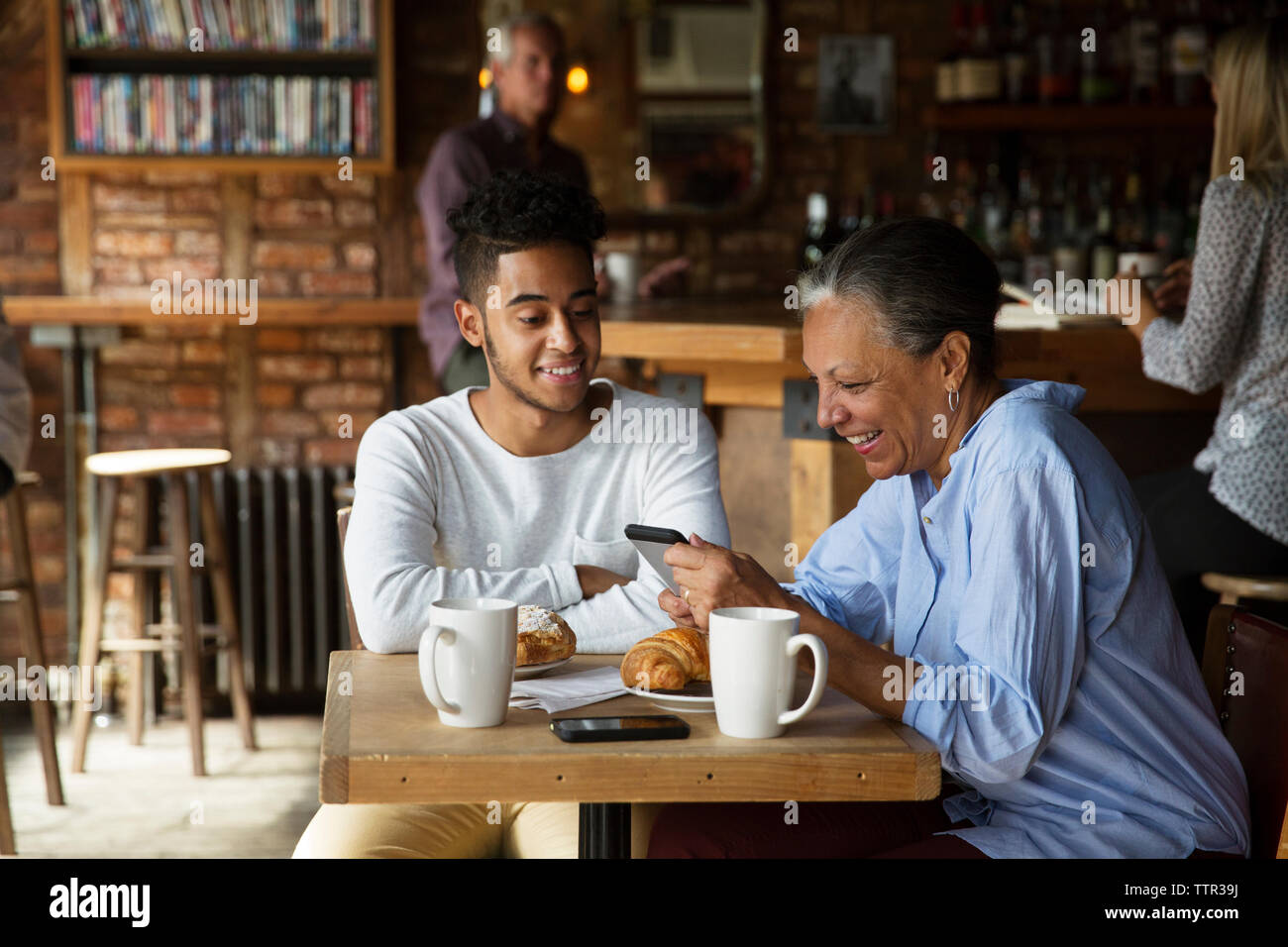 Lächelnd Mann auf Frau mit Telefon, während Kunden Entspannung im Cafe Stockfoto