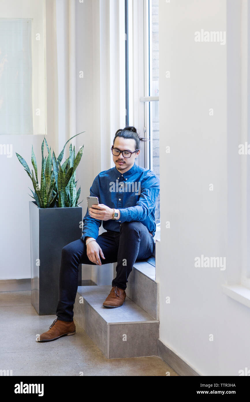 Geschäftsmann, der das Handy benutzt, während er im Büro vor der Tür sitzt Stockfoto