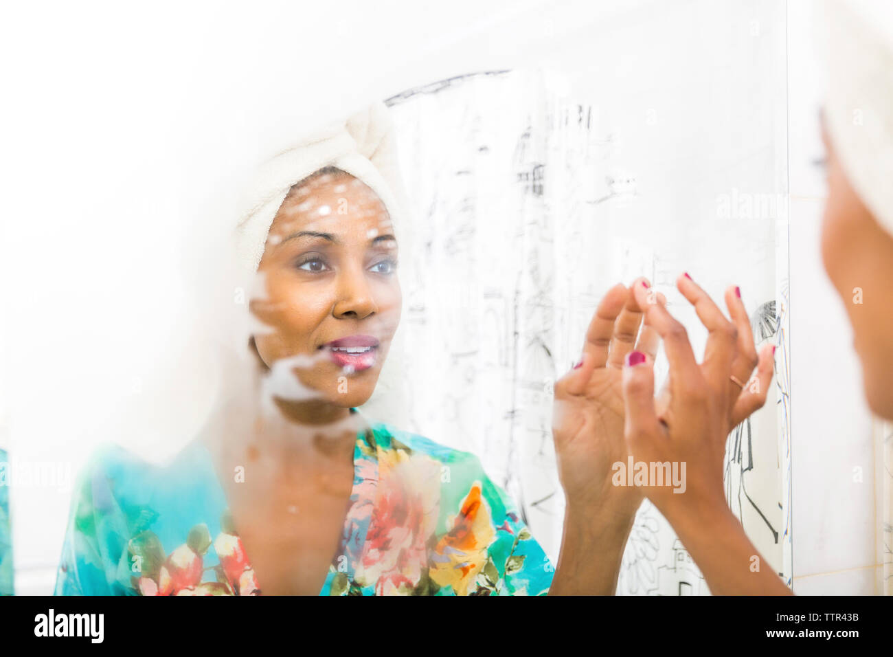 Frau mit Handtuch auf dem Kopf, während sie an der Reflexion im Spiegel Stockfoto